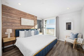 Een moderne slaapkamer met een groot bed, houten wandbekleding, uitzicht op het strand en een zithoekje.