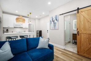 A modern living room with a blue sofa, a kitchen area with white cabinets, and a wooden sliding door. - West Oceanfront Oasis 2-3-4-6-7 (Newport Beach)