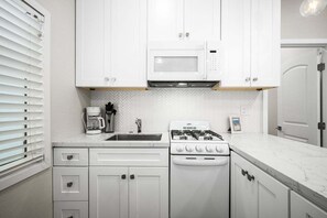 A kitchen with white cabinets, a microwave, a stove, a sink, and a coffee maker. - West Oceanfront Oasis 2-3-4-6-7 (Newport Beach)