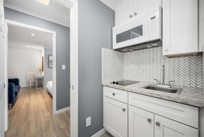 Een moderne keuken met witte kastjes, een backsplash van mozaïektegels in een visgraatpatroon, en een inbouwmagnetron.