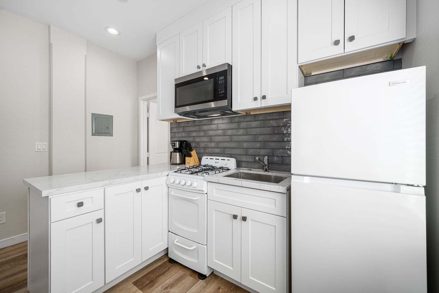 Una cocina moderna con armarios blancos, estufa a gas, microondas y refrigerador.