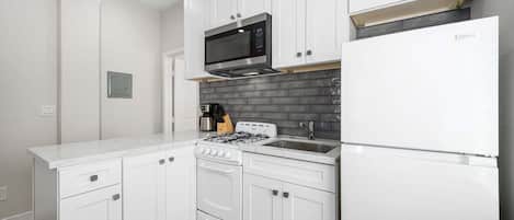 Una cocina moderna con armarios blancos, estufa a gas, microondas y refrigerador.