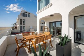 Ein modernes Gebäude mit einem Balkon, einem Essbereich mit Holzmöbeln und Blick auf den Strand.