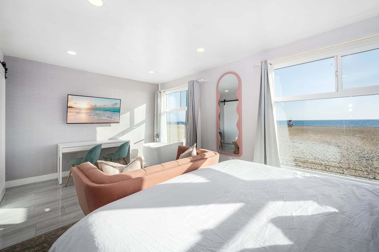 Un dormitorio con una cama grande, un escritorio, una silla, un espejo y vista a la playa.