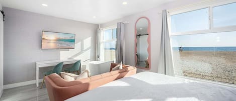Un dormitorio con una cama grande, un escritorio, una silla, un espejo y vista a la playa.