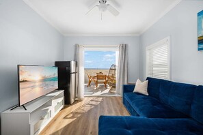 A modern living room with a television, a blue sofa, and a view of the beach through an open door. - West Oceanfront Oasis 1-5-8-9 (Newport Beach)