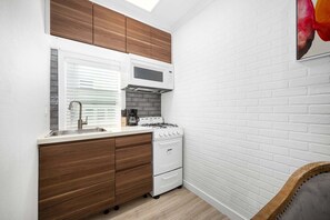 A compact kitchen with white brick walls, wooden cabinets, a gas stove, and a sink. - West Oceanfront Oasis 1-5-8-9 (Newport Beach)