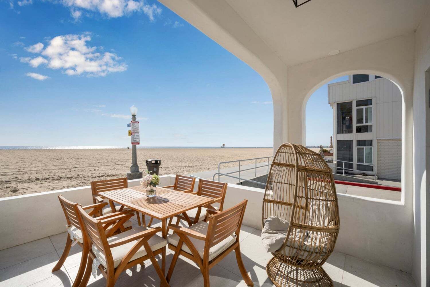 A beachside patio with a table and chairs, a wicker chair, and a view of the beach and ocean.
