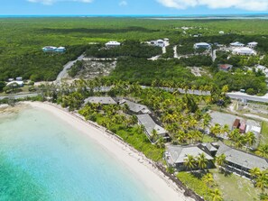 Eine Luftaufnahme eines Küstenresorts mit mehreren Gebäuden, einem Strand und üppiger tropischer Vegetation.
