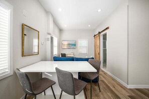 A modern dining area with a white table, four chairs, a blue sofa, and a painting on the wall. - West Oceanfront Oasis 3-4-5-6-9 (Newport Beach)