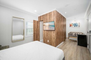 Ein Schlafzimmer mit einem Bett, einer Wand im Holzoptik, einem Fernseher, einem Sofa und einem kleinen Schrank.