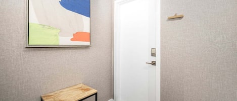Un pasillo con una puerta blanca, una pequeña mesa de madera y un cuadro abstracto de colores en la pared.