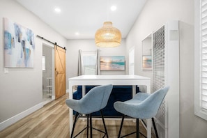 Ein modernes Interieur mit einem weißen Tisch, zwei blauen Barhocker, einer Pendelleuchte und Kunstwerken an den Wänden.