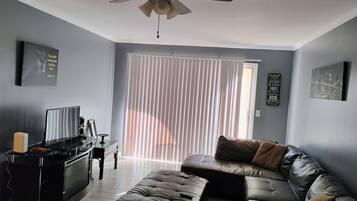 A living room with a sectional sofa, a ceiling fan, a TV, and a fireplace.