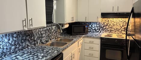 A kitchen with white cabinets, a granite countertop, a black microwave, a stove, and a dishwasher.
