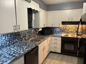 A kitchen with white cabinets, a granite countertop, a black microwave, a stove, and a dishwasher.