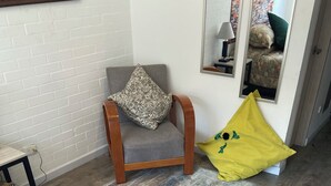 A room with a wooden floor, a grey armchair with a patterned cushion, a yellow cushion with a green design, a floral-patterned bedspread, and a mirror on the wall. - A Sober and Elegant Loft Apartment in Chapinero (Bogotá)