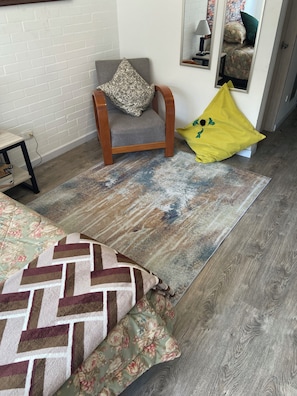 A room with a wooden floor, a grey armchair with a patterned cushion, a yellow cushion with a green design, a floral-patterned bedspread, and a mirror on the wall. - A Sober and Elegant Loft Apartment in Chapinero (Bogotá)