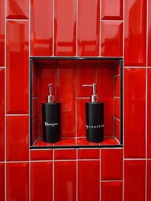 A bathroom with red tiled walls and two black dispensers labeled 'Shampoo' and 'Conditioner' in a rectangular alcove. - La Presentosa Studio Apartment (Bologna)