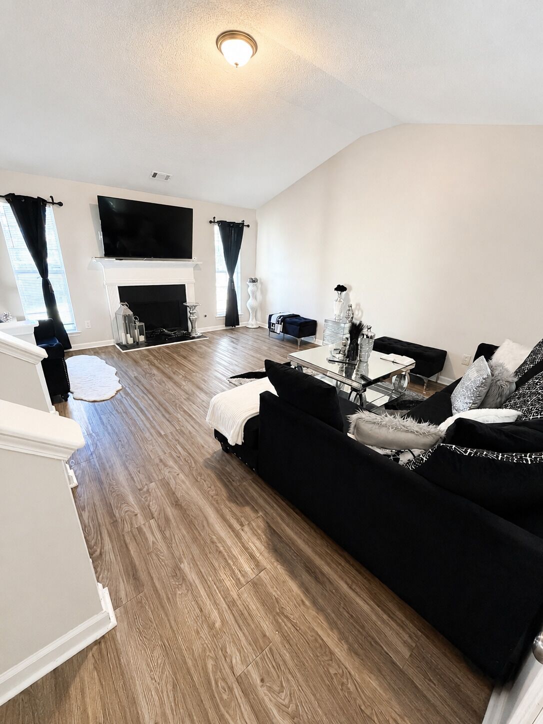 A modern living room with a fireplace, a black sofa, a coffee table, and a flat-screen TV mounted above the fireplace.