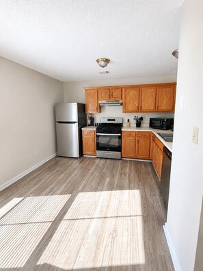 A kitchen with wooden cabinets, stainless steel appliances, and a light-colored floor. - Charming 3-bedroom house with AC in pleasant Riverdale (Riverdale)