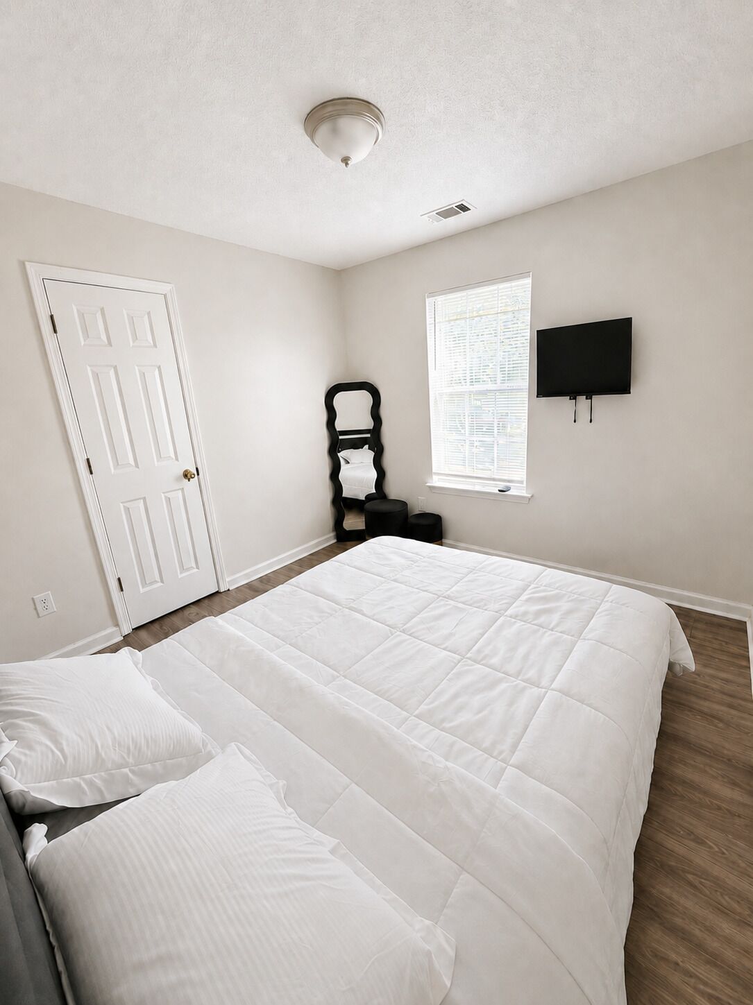 A bedroom with a bed, a chair, a television, and a window.