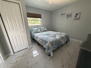 A bedroom with a bed, a window with blinds, a door, and a wall with three pictures. - Blue Water Palms • Heated Pool • Beaches & River (Palm Bay)