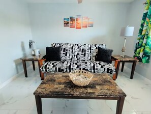 A living room with a patterned sofa, a coffee table, a wall-mounted lamp, and a framed artwork above the sofa. - Blue Water Palms • Heated Pool • Beaches & River (Palm Bay)