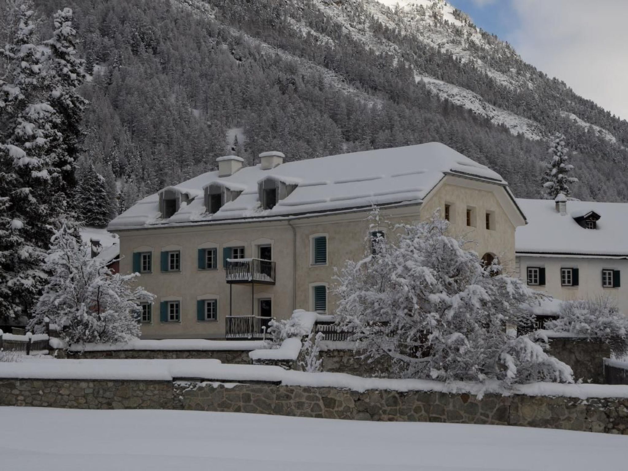 A large building with multiple windows and balconies, surrounded by snow-covered trees and mountains.
