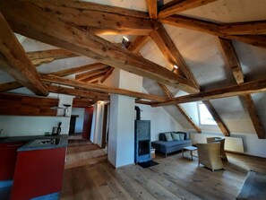 A loft-style room with exposed wooden beams, a fireplace, a sofa, and a kitchen area. - Chesa Tach by Interhome (Bever)
