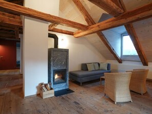A loft bedroom with a stone fireplace, wooden beams, a grey sofa, and wicker chairs. - Chesa Tach by Interhome (Bever)
