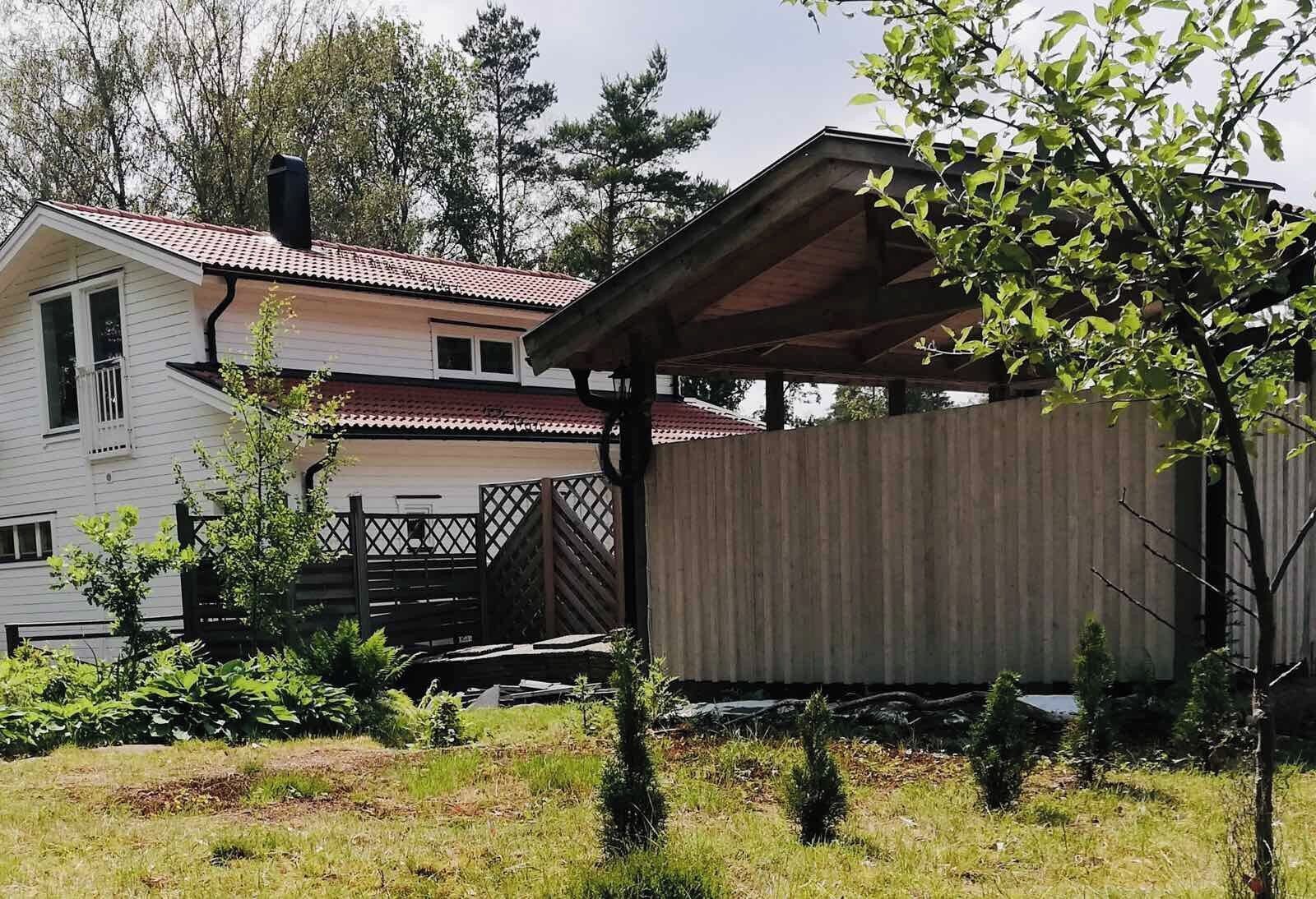 En bostadsfastighet med en inglasad veranda, en inhägnad trädgård och ett hus med ett rött tegeltak.