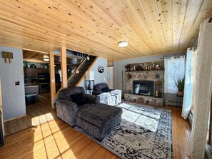 A cozy living room with a fireplace, a sofa, and a staircase leading to an upper level. - Northern Escape | Sauna, Dock & Lake Access (Butternut)