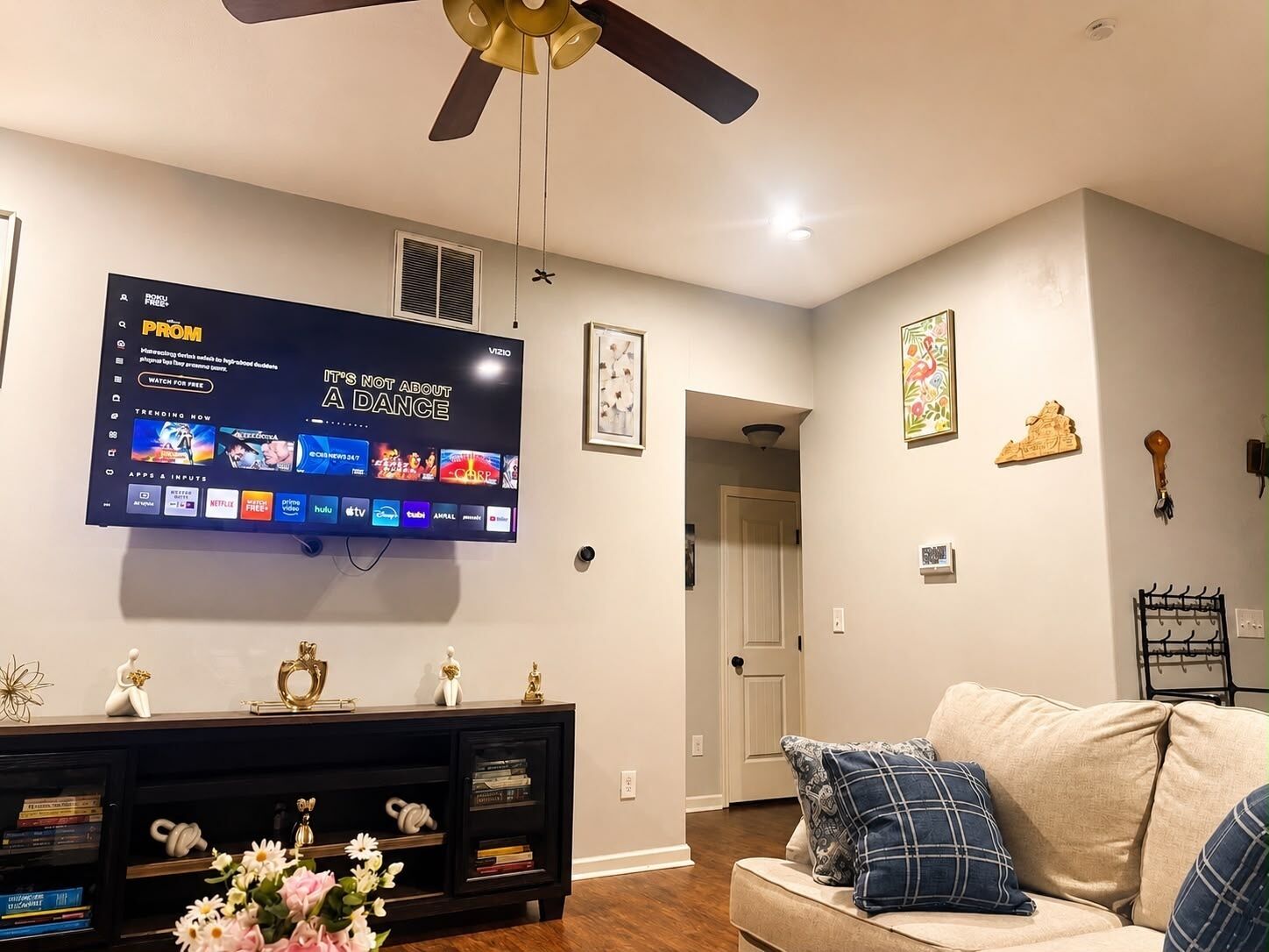 A living room with a flat-screen TV mounted on the wall, a ceiling fan, a sofa, and a coffee table.