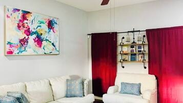 A living room with a ceiling fan, a white sofa, a coffee table, and a red curtain.
