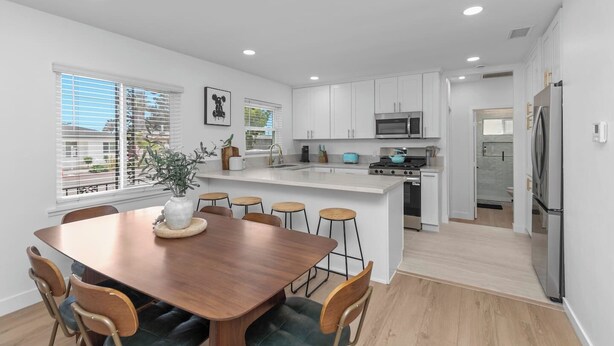 Une cuisine moderne avec des meubles blancs, un îlot central et un coin repas comprenant une table et des chaises en bois.