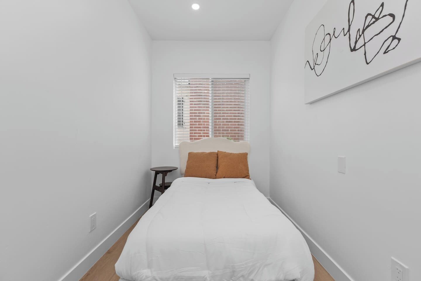 Un dormitorio con cama, una mesita, una ventana con persianas y una pared con un letrero.