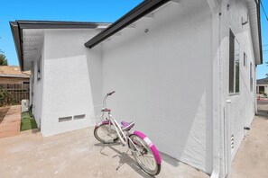 A white building with a single door and a window, a pink bicycle parked against it, and a clear blue sky. - Modern San Diego Home, Sleeps 8 w/ Parking (San Diego)
