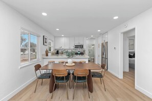 A modern kitchen with white cabinets, a central island, and a dining area with a wooden table and chairs. - Modern San Diego Home, Sleeps 8 w/ Parking (San Diego)