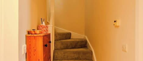 A narrow hallway with a wooden cabinet and a carpeted staircase.