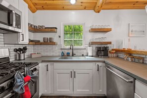 A modern kitchen with white cabinets, a stainless steel stove, and a wooden ceiling. - Cozy modern cabin in Lower Moonridge, 5 minutes from Big Bear Mountain! (Big Bear Lake)