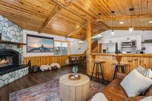 Um interior aconchegante com lareira de pedra, teto de madeira, espaço para bar e cozinha.
