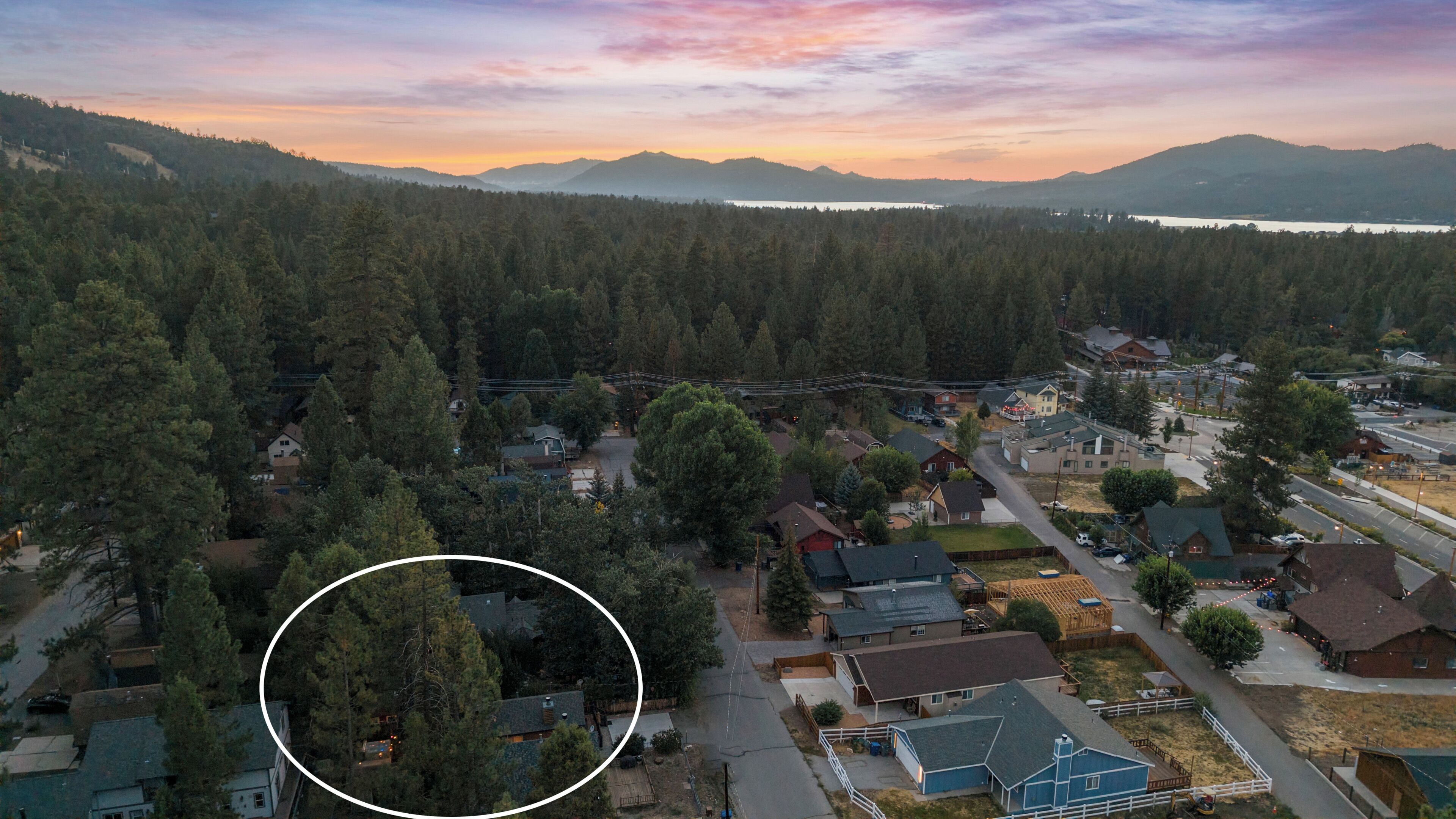 An aerial view of a residential area with houses, roads, and a forested backdrop.