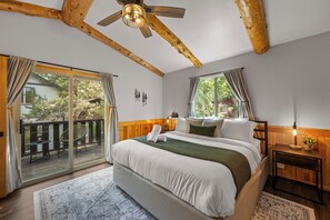 A bedroom with a large bed, a wooden ceiling, and a view of the outdoors through a sliding glass door. - Cozy modern cabin in Lower Moonridge, 5 minutes from Big Bear Mountain! (Big Bear Lake)