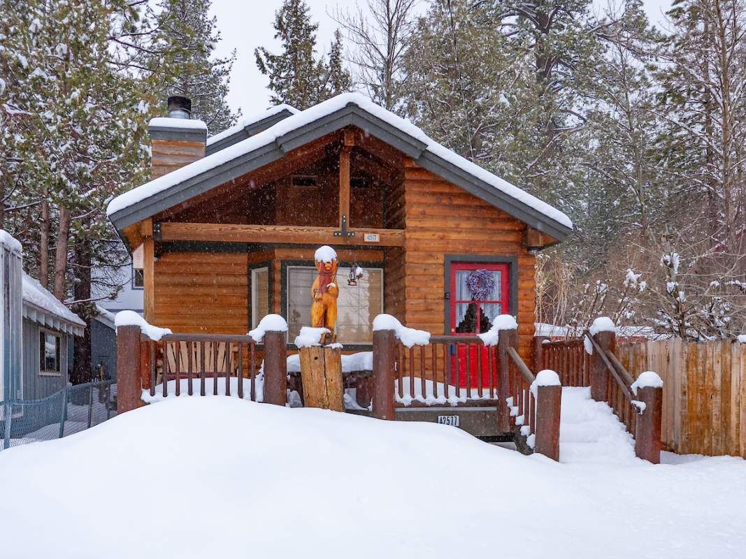 A wooden cabin with a red door, surrounded by snow-covered trees.