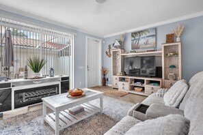 Een woonkamer met een televisie, bank, salontafel en uitzicht op het buiten.