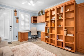 Ein Zimmer mit Schreibtisch, Bürostuhl und einer großen, hölzernen Bücherwand voller Bücher.