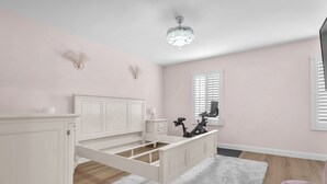 Ein Schlafzimmer mit einem weißen Bett, einem flauschigen Teppich, einem Fenster mit Jalousien und einer Deckenleuchte.