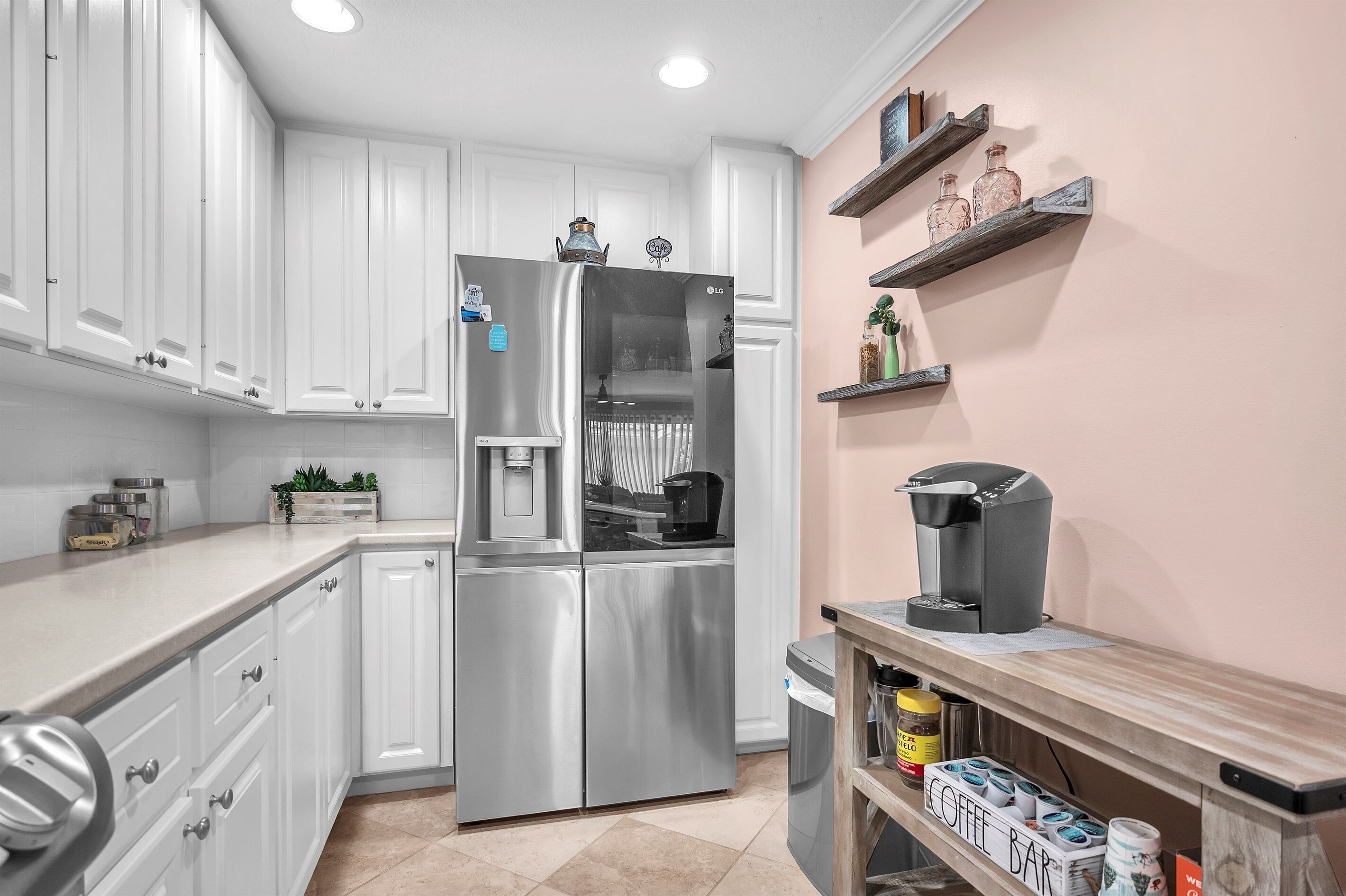 A modern kitchen with white cabinetry, a stainless steel refrigerator, a coffee machine, and a coffee bar.