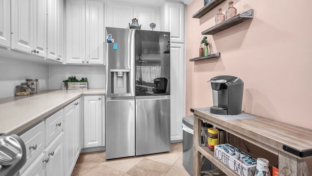 Eine moderne Küche mit weißen Schränken, einem Edelstahlkühlschrank, einer Kaffeemaschine und einer Kaffeobar.